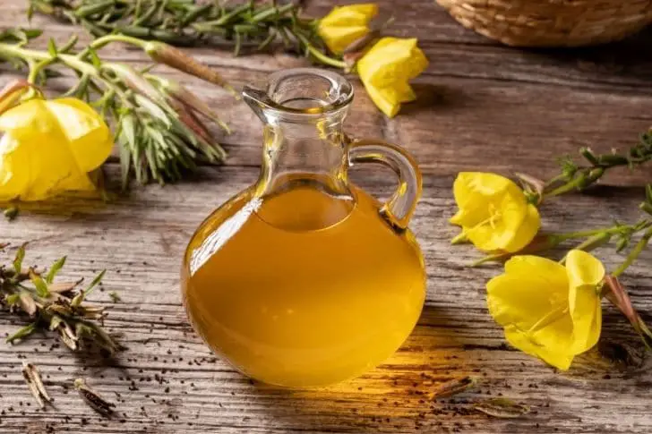 Jarra con aceite de onagra sobre mesa de madera. Flores de onagra.