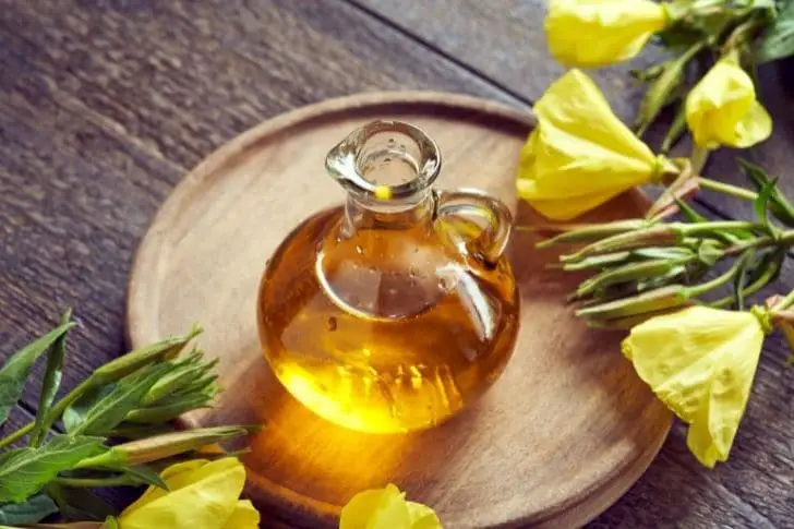 Tabla de madera con jarra con aceite de onagra y flores de onagra.