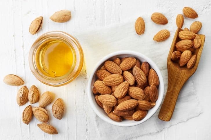 Aceite de almendras para las pestañas en un tarro de cristal junto a almendras.